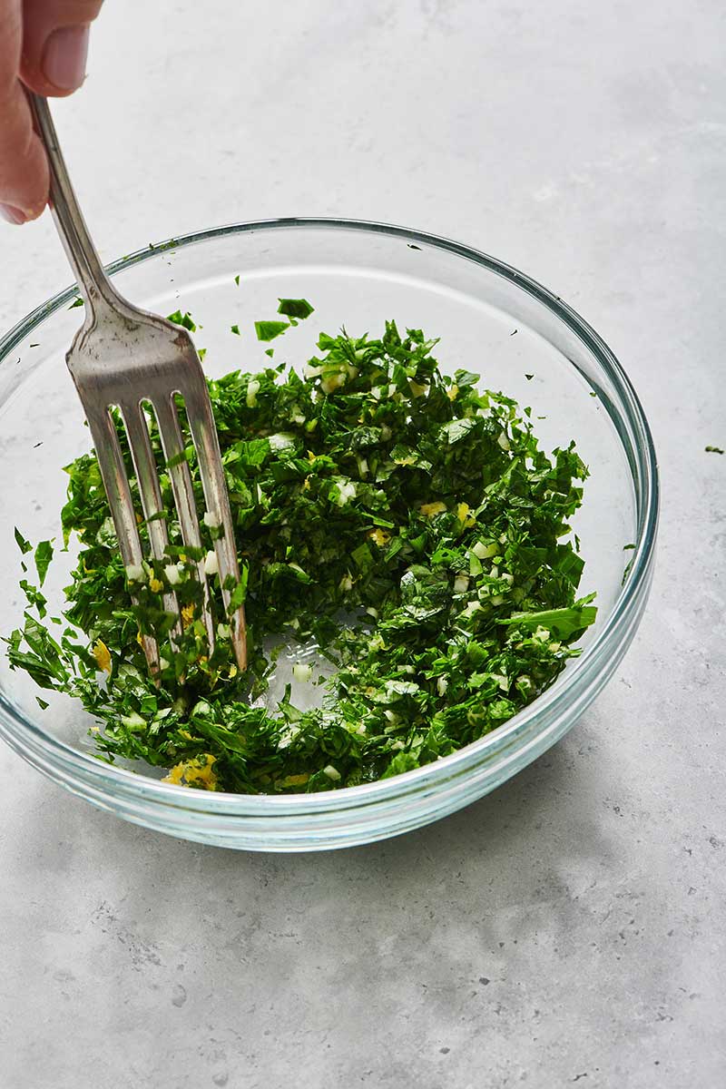 Woman mashing herbs and zest for gremolata with a fork. 