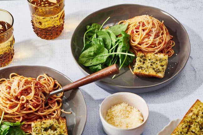 Table setting with spaghetti and homemade marinara sauce, lettuce, and garlic bread