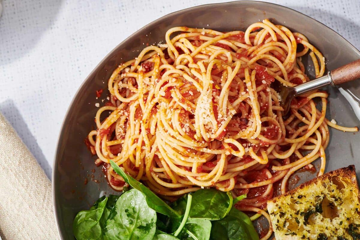 Spaghetti with homemade marinara sauce on plate with salad and garlic bread.