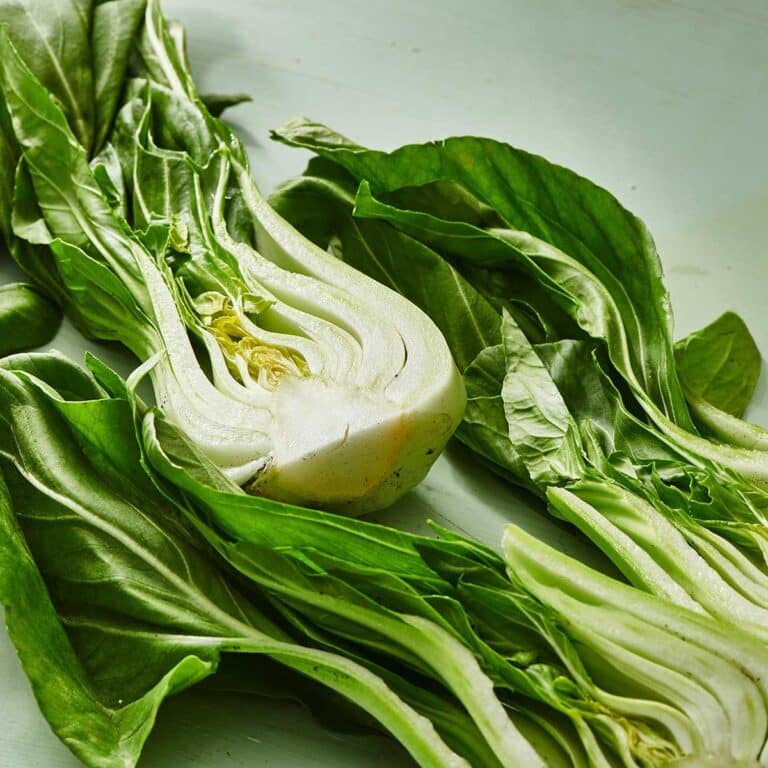 Baby bok choy cut in half, sitting on green surface.