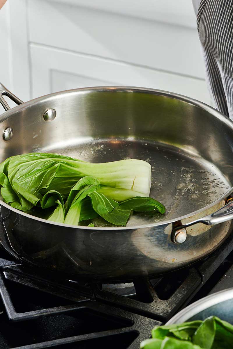 Halved Baby Bok Choy in a pan on the stove.