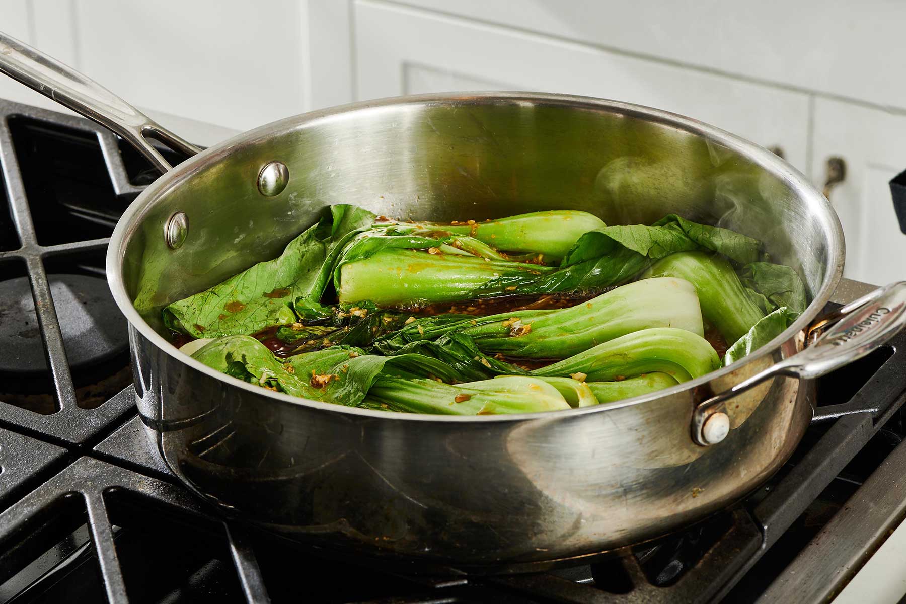 Baby Bok Choy simmering in a pan with a soy sauce and broth mixture.