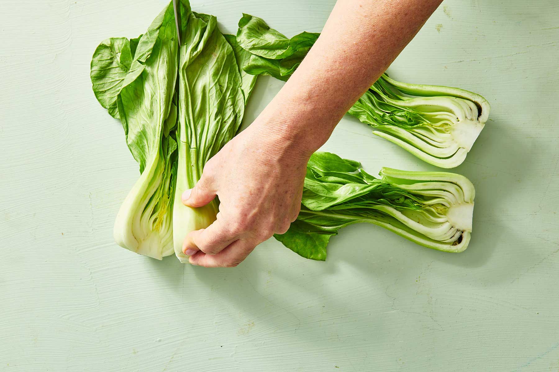 Person using a knife to slice baby bok choy lengthwise.