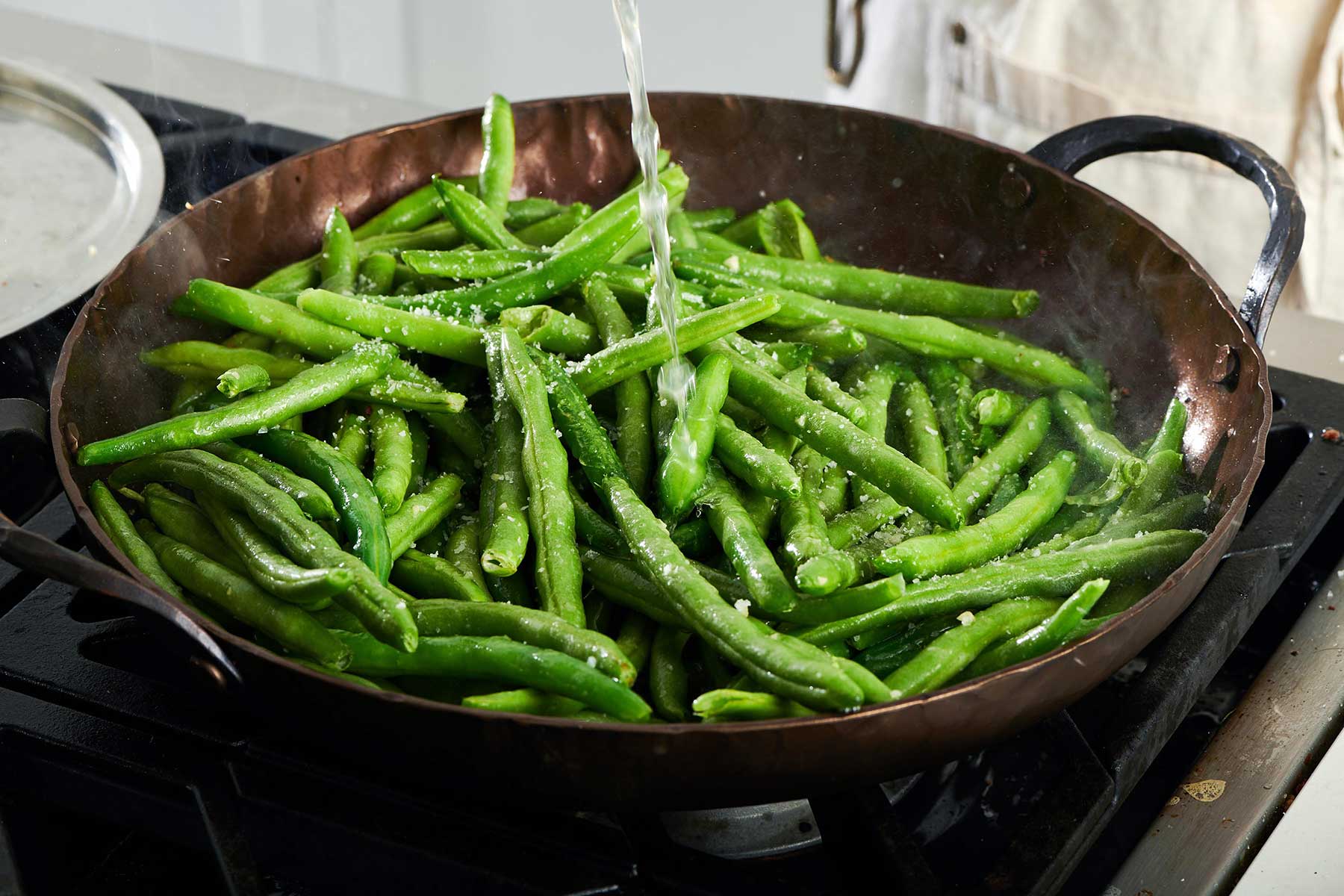 Water pouring into a skillet of seasoned green beans.