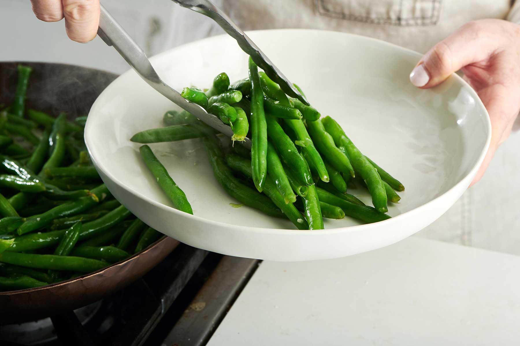 Using tongs to place Cook Fresh Green Beans on plate.
