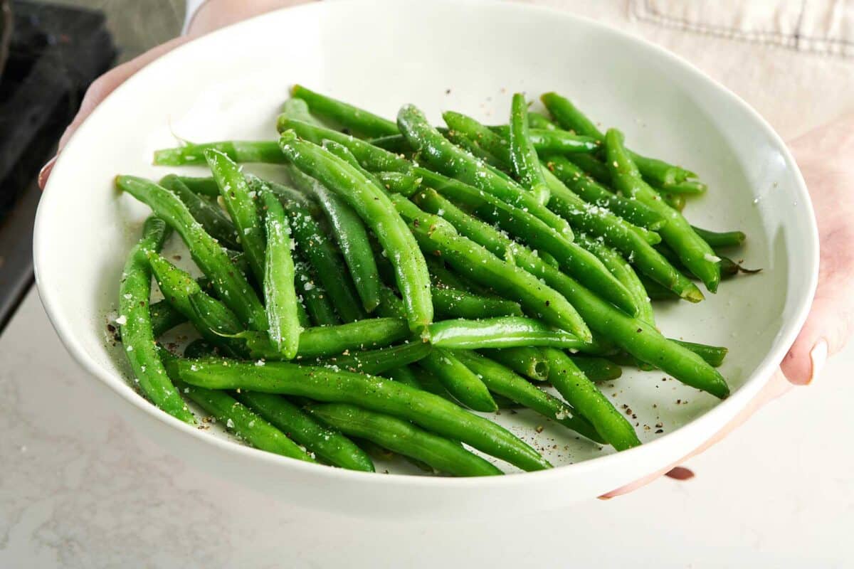 Green beans topped with salt and pepper on a white plate.