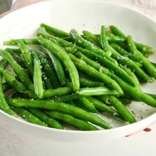 Green beans topped with salt and pepper on a white plate.