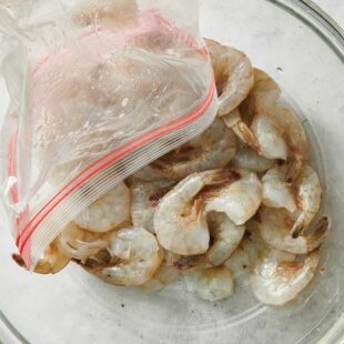 Shrimp being poured from a bag into a glass bowl.