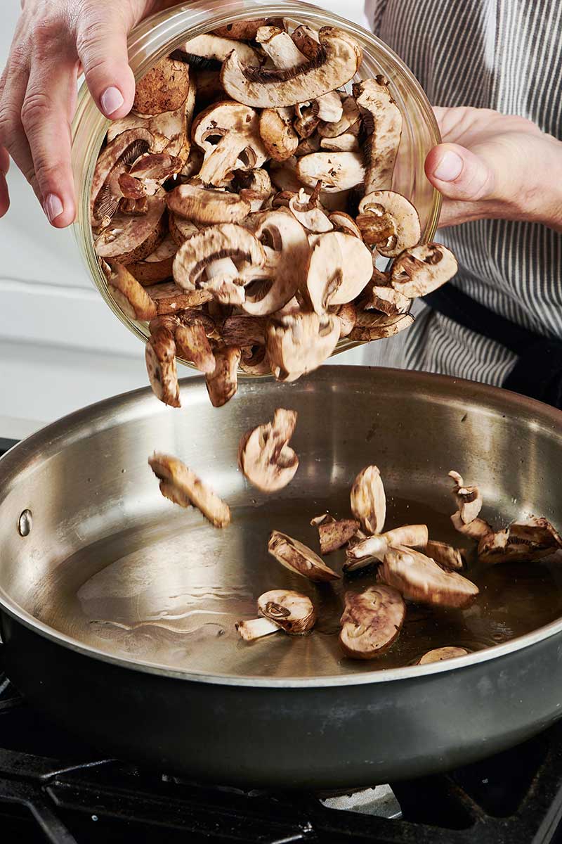 Woman adding mushrooms to a skillet.
