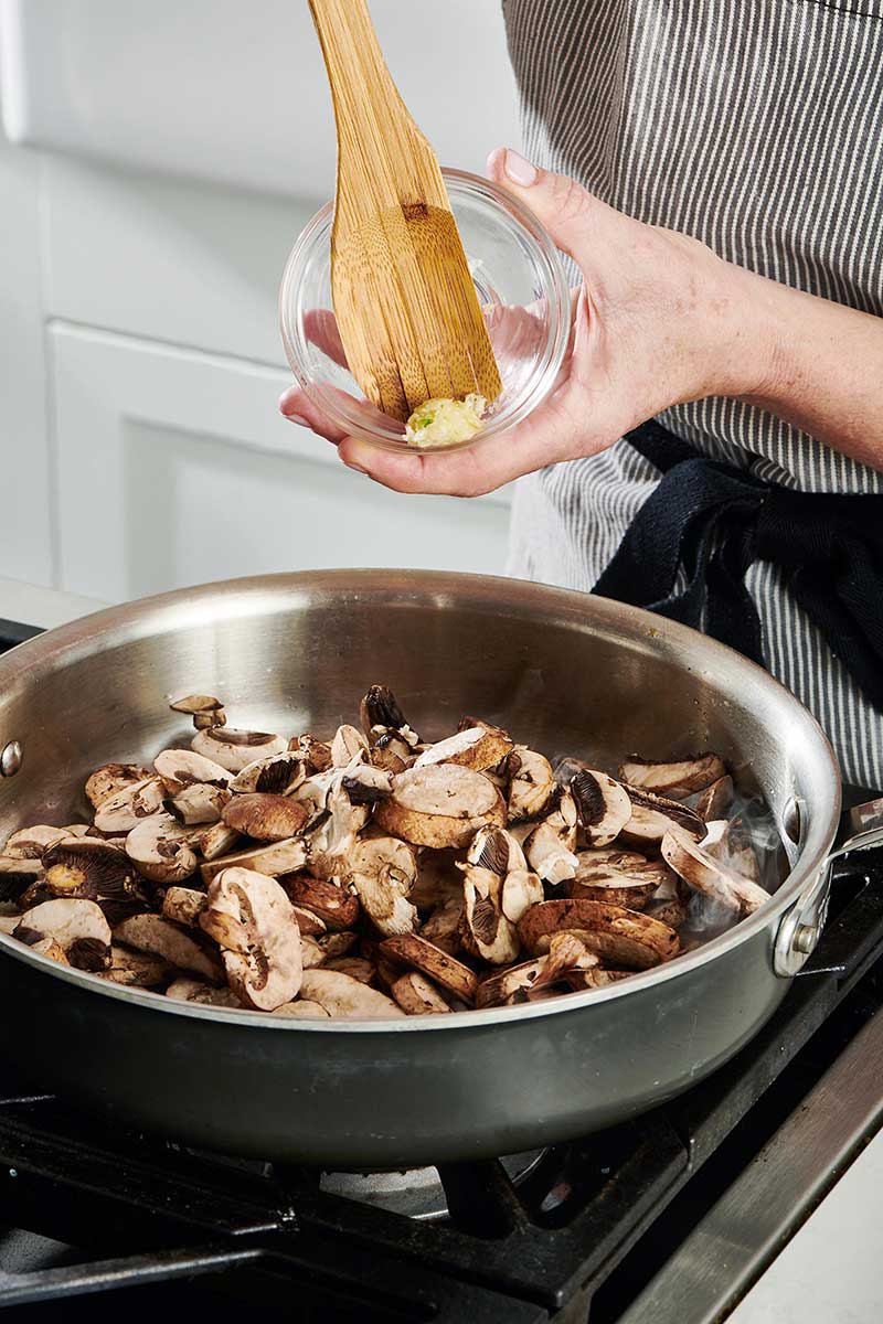 Woman adding garlic to mushrooms in a pan.