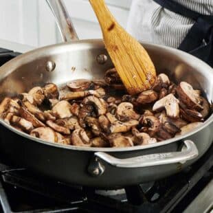 Sauteing mushrooms in large skillet and stirring with wood spoon.