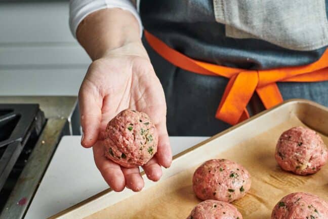 Woman holding freshly formed Jumbo Meatball before baking on parchment-lined pan.