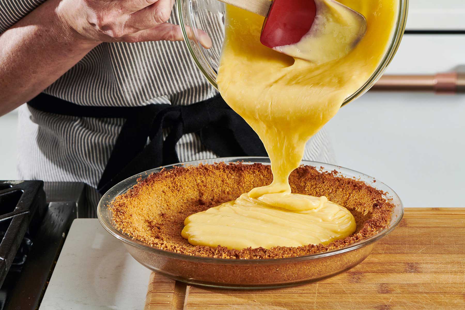Pouring pie filling from a bowl into a baked pie crust.