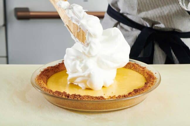 Wooden spoon scooping meringue onto a Key Lime Pie.
