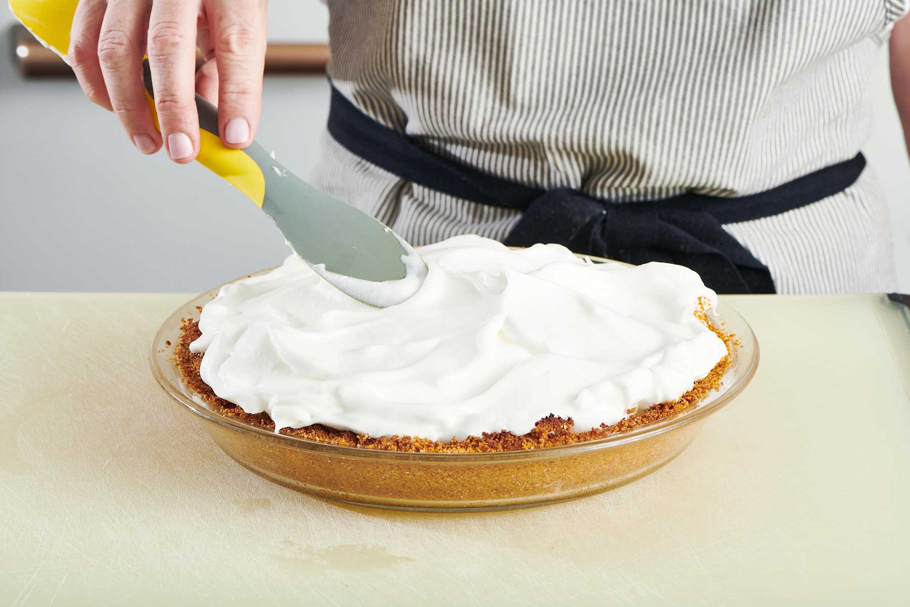 Spatula spreading meringue onto a Key Lime Pie.