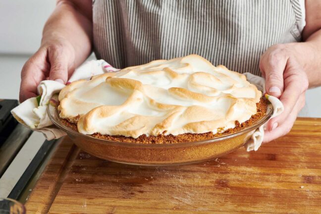 Hands holding a Key Lime Pie in a glass pie dish.