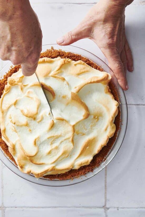 Hands about to use a knife to cut into a Key Lime Pie.