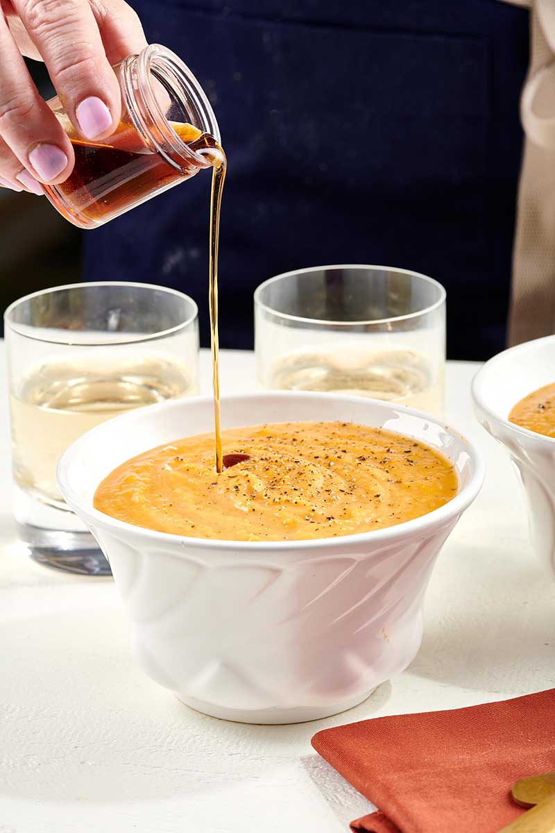 Woman drizzling maple syrup onto butternut squash soup.