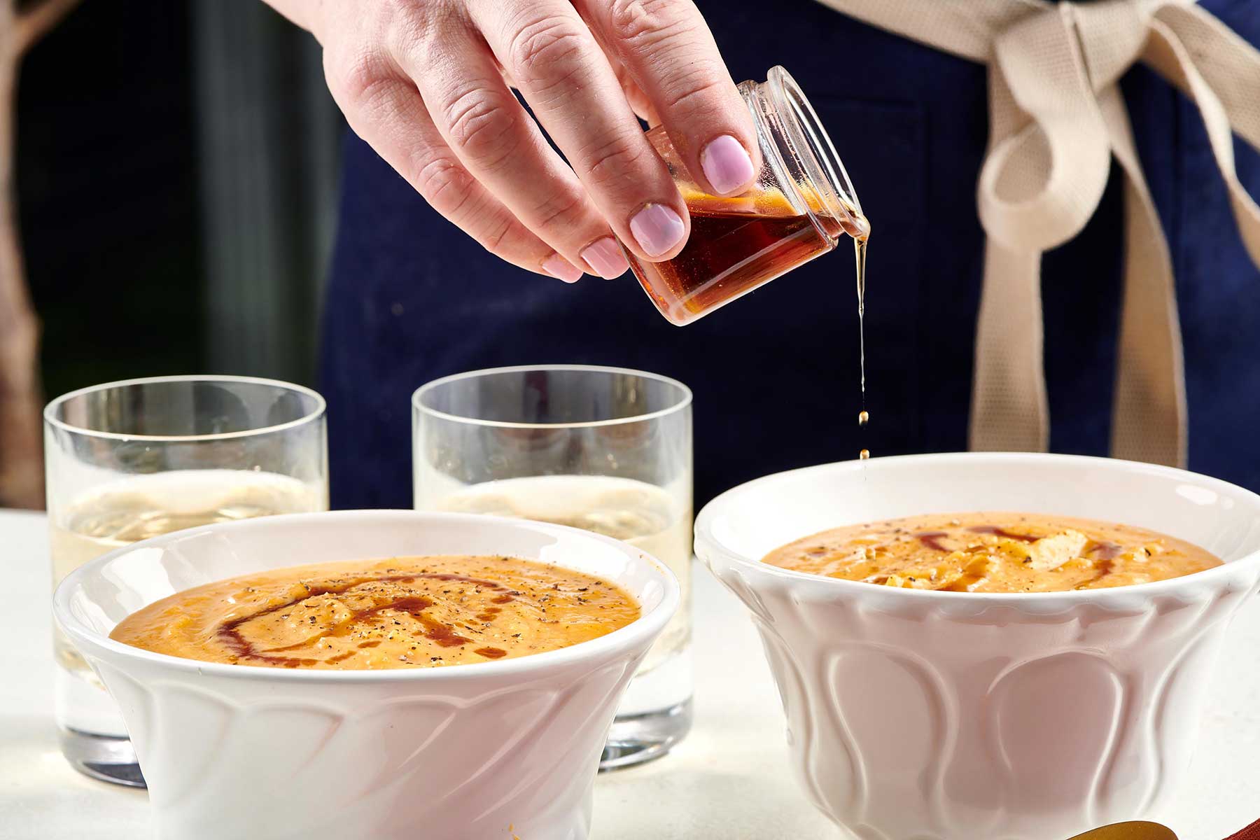 Pouring maple syrup over butternut squash soup in white bowls.