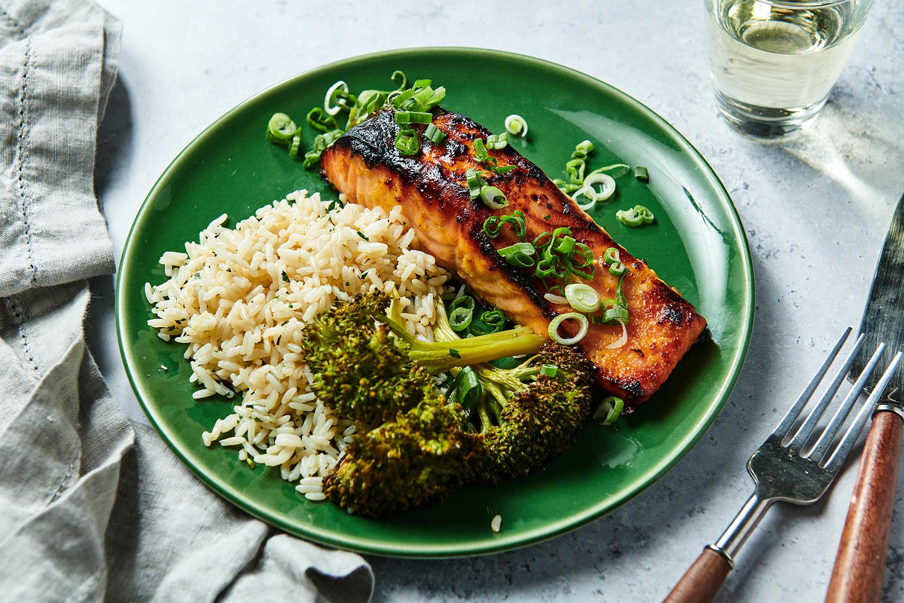 Table setting with broiled Miso Salmon on green plate with broccoli and rice.