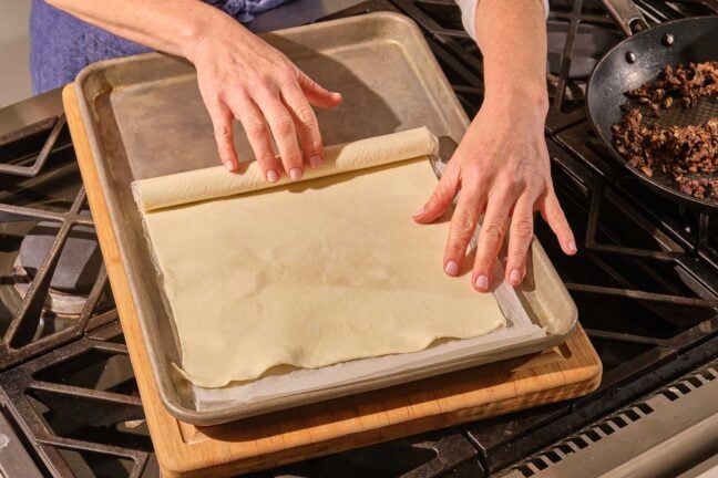 Woman unrolling puff pastry onto a baking sheet.