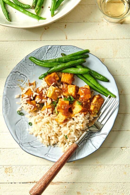 Orange tofu with rice and green beans on plate
