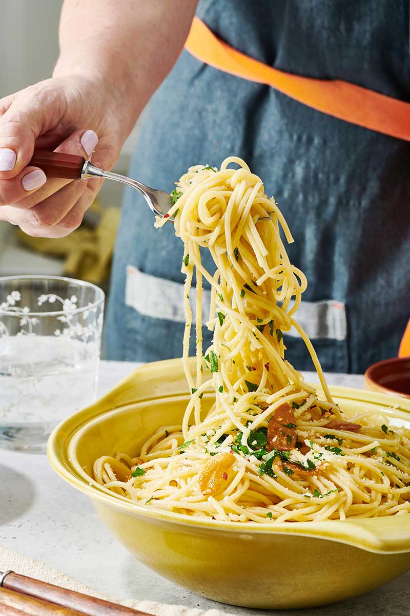 Woman serving Pasta Aglio e Olio with fork.