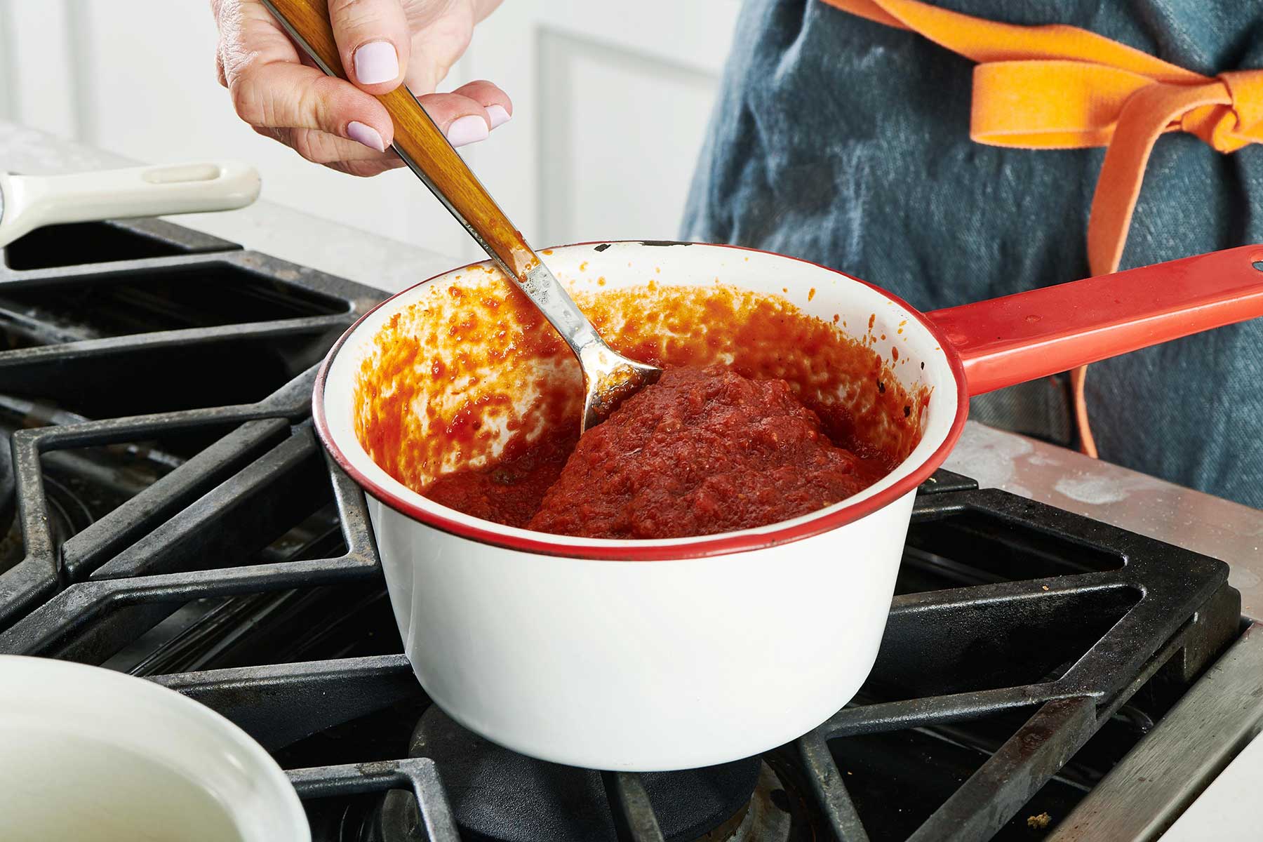 Woman stirring Puttanesca tomato-based sauce in white pan on the stove.
