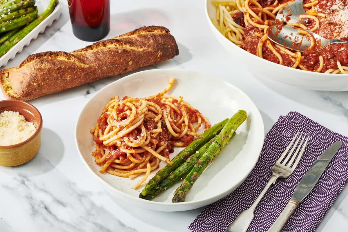 Table setting featuring Pasta Puttanesca on plate with grilled asparagus and garlic bread.