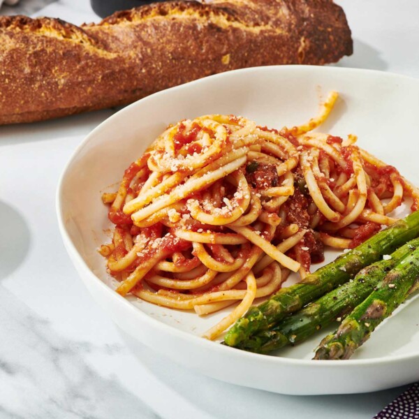 Pasta Puttanesca and asparagus on a plate next to loaf of bread.
