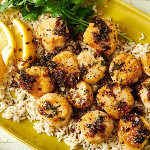 Seared scallops on yellow plate over rice with lemon wedges.