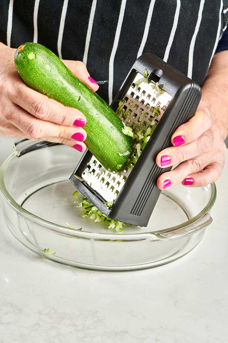 Woman grating zucchini with box grater.