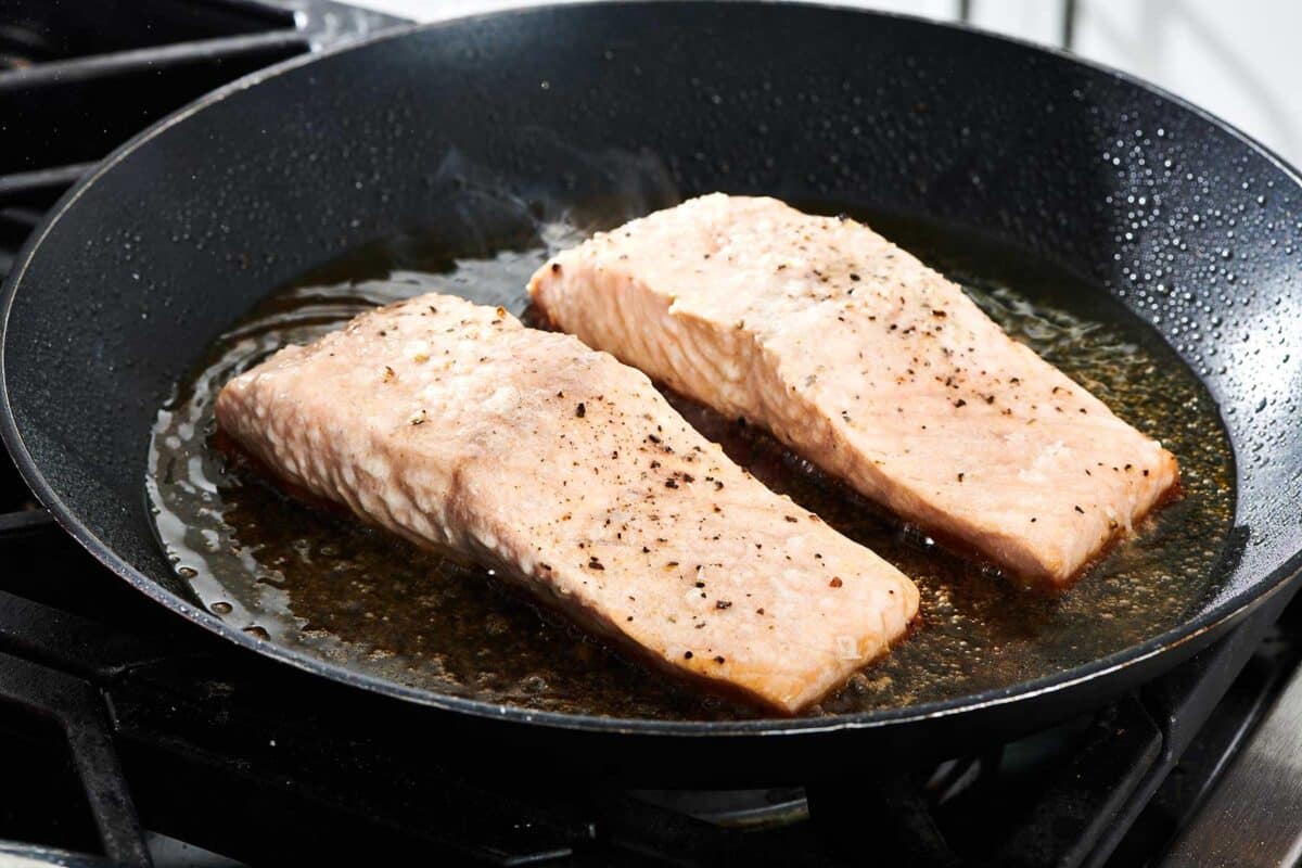 Cooking salmon filets in pan on stove.