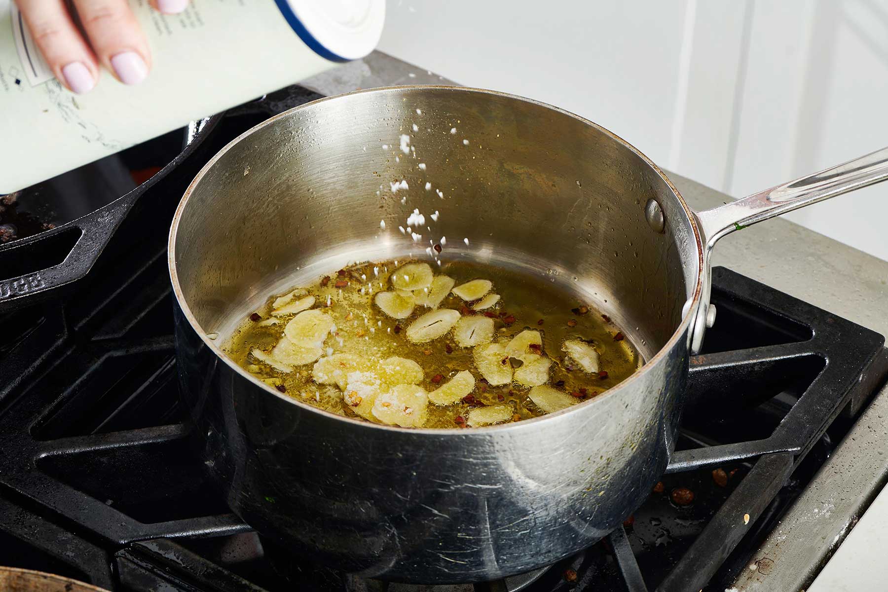 Woman salting sauteed garlic in a pot on the stove.