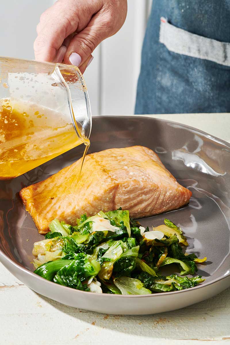 Pouring lemon butter over salmon with sauteed escarole.