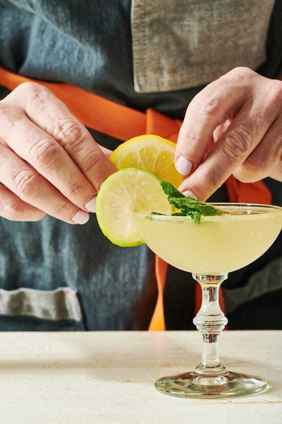 Hands putting a lemon slice on a rim of a Sparkling Limoncello Cocktail.