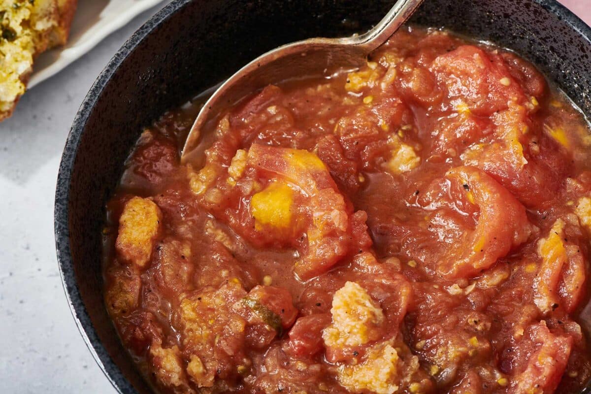 Spoon dipping into Stewed Tomatoes in a pan.