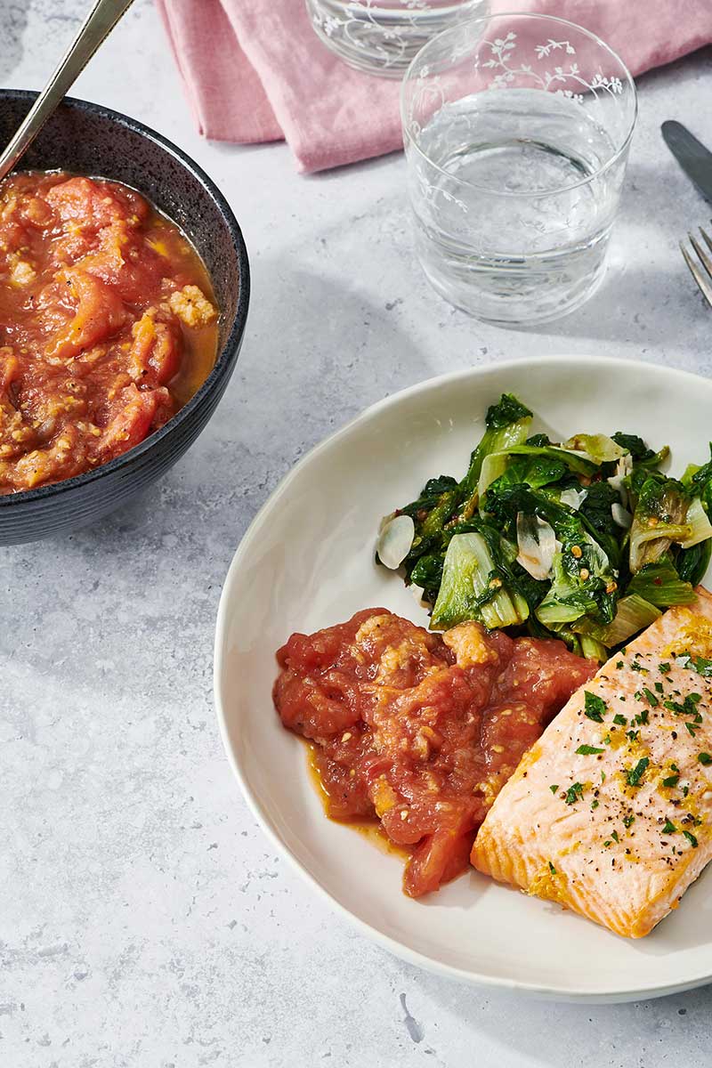 Stewed Tomatoes with sautéed greens and fish fillet on a plate.