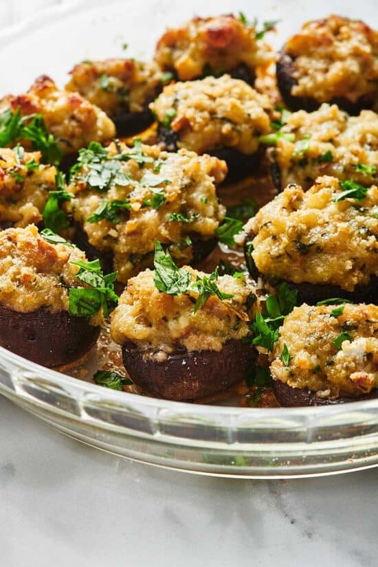 Stuffed Mushrooms topped with chopped parsley in a glass bowl.