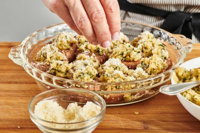 Hand sprinkling Parmesan cheese onto a bowl of Stuffed Mushrooms.