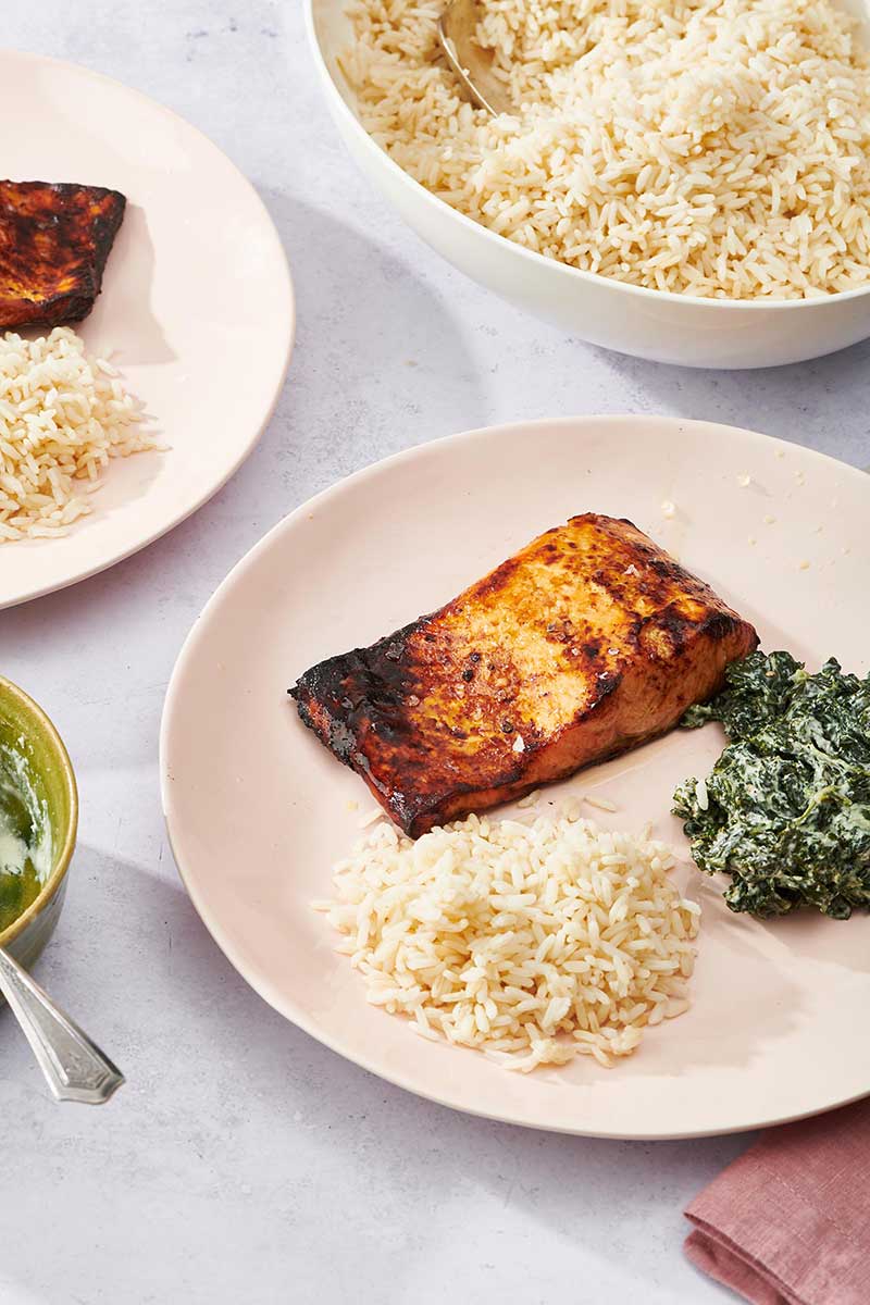 Air Fryer Salmon on pink plate with rice and creamed kale side dishes.