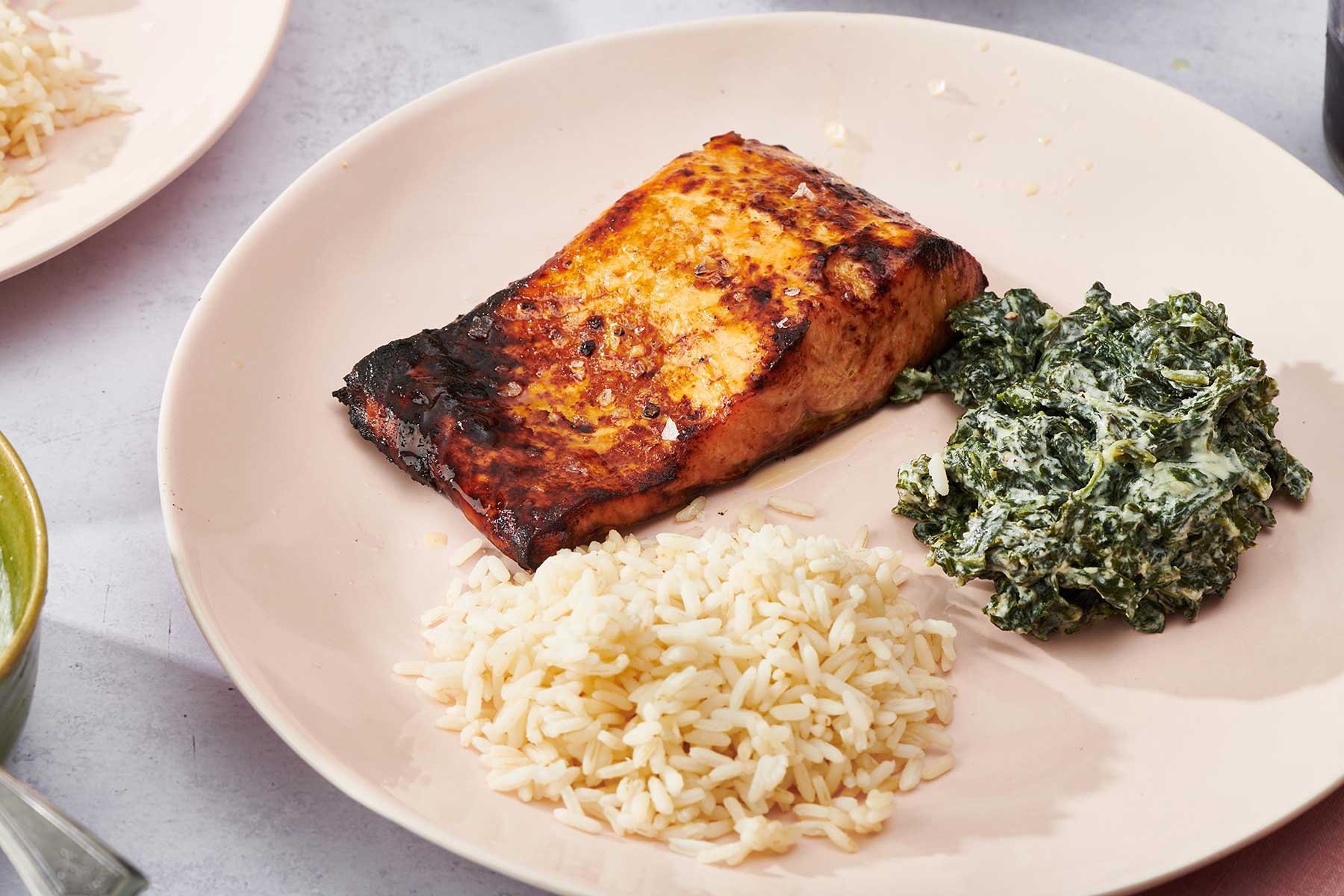 Salmon filet cooked in air fryer on plate with creamed greens and rice.