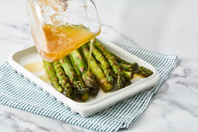 Pouring lemon butter sauce over grilled asparagus