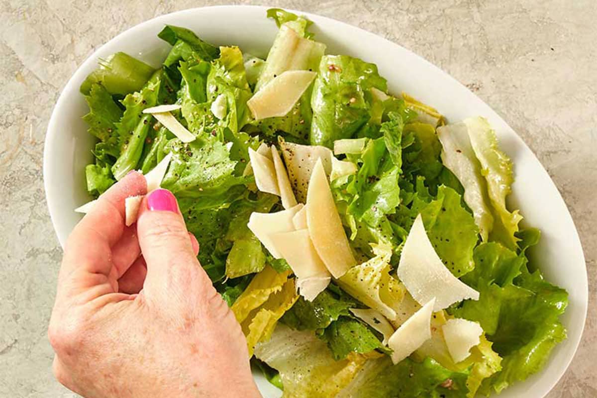 Hand sprinkling parmesan shavings onto an Escarole Salad.