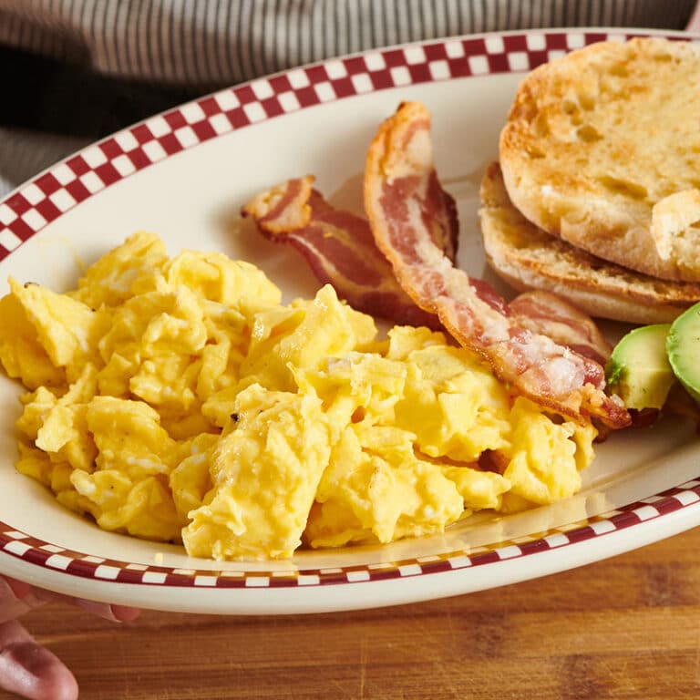 Scrambled eggs with bacon and English muffin on plate
