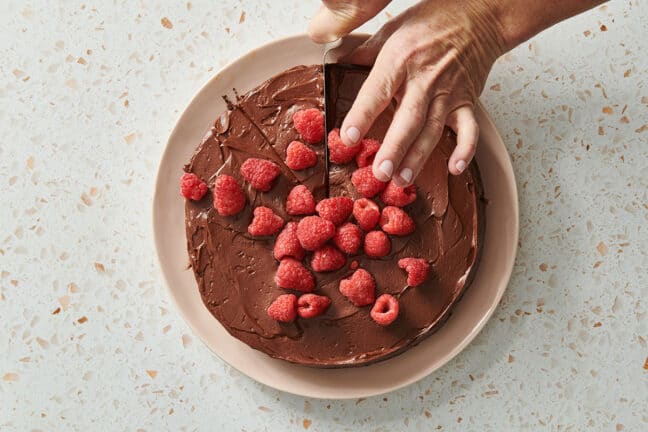 Slicing chocolate cake with raspberries