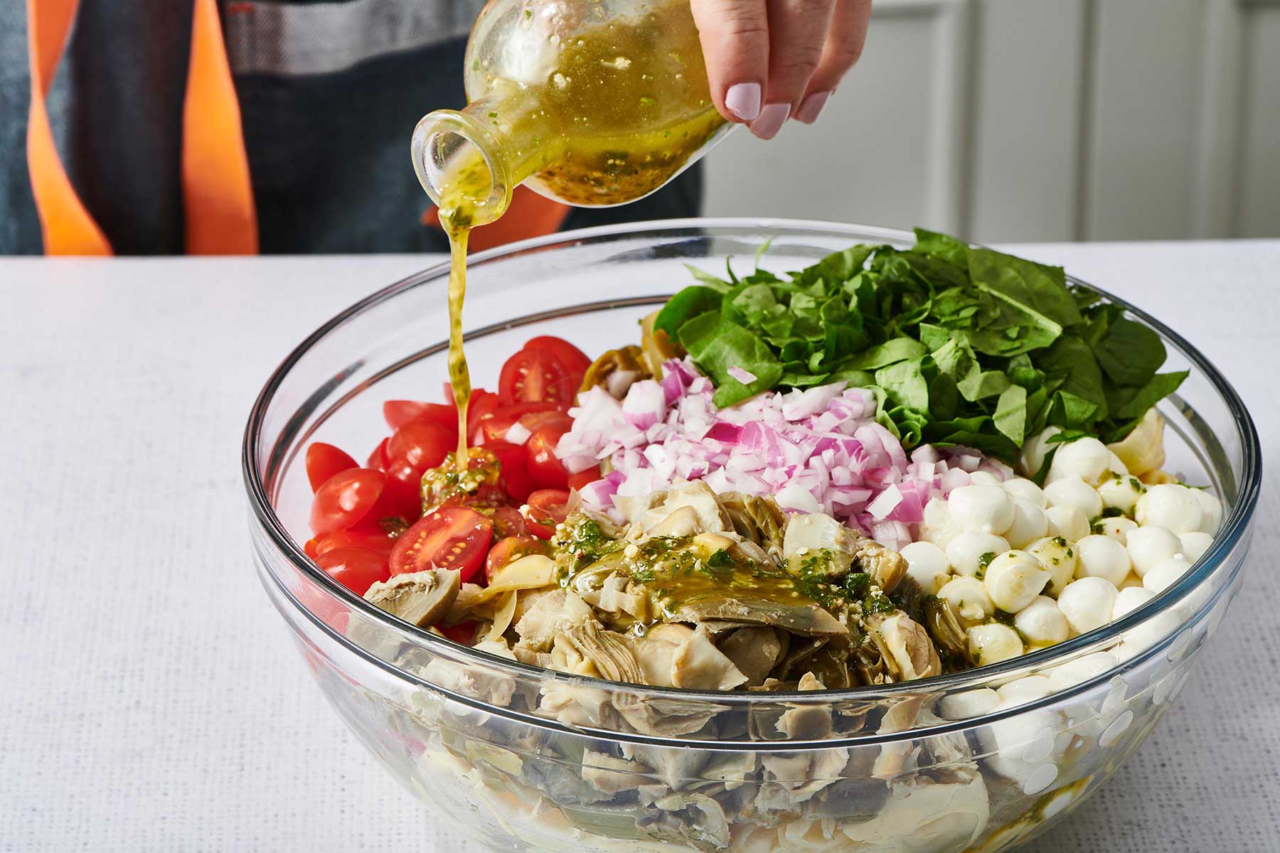 Woman pouring pesto and olive oil dressing over a bowl of Tortellini Pasta Salad.