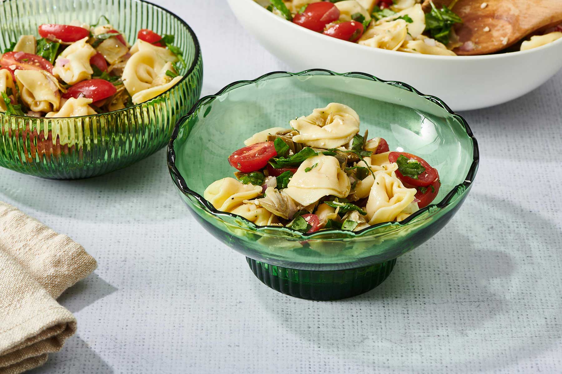 Green glass bowls filled with Tortellini Pasta Salad.
