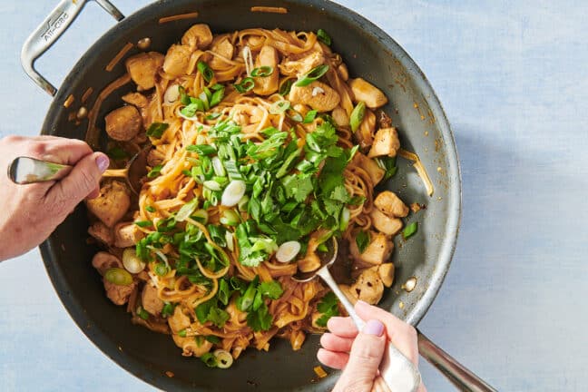 Stir-frying chicken, rice noodles, and scallions in wok