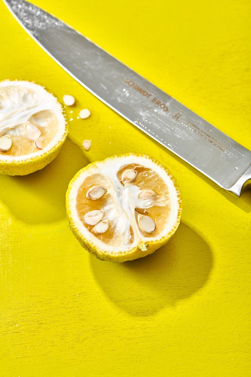 Cut yuzu fruit with chef knife on yellow table.